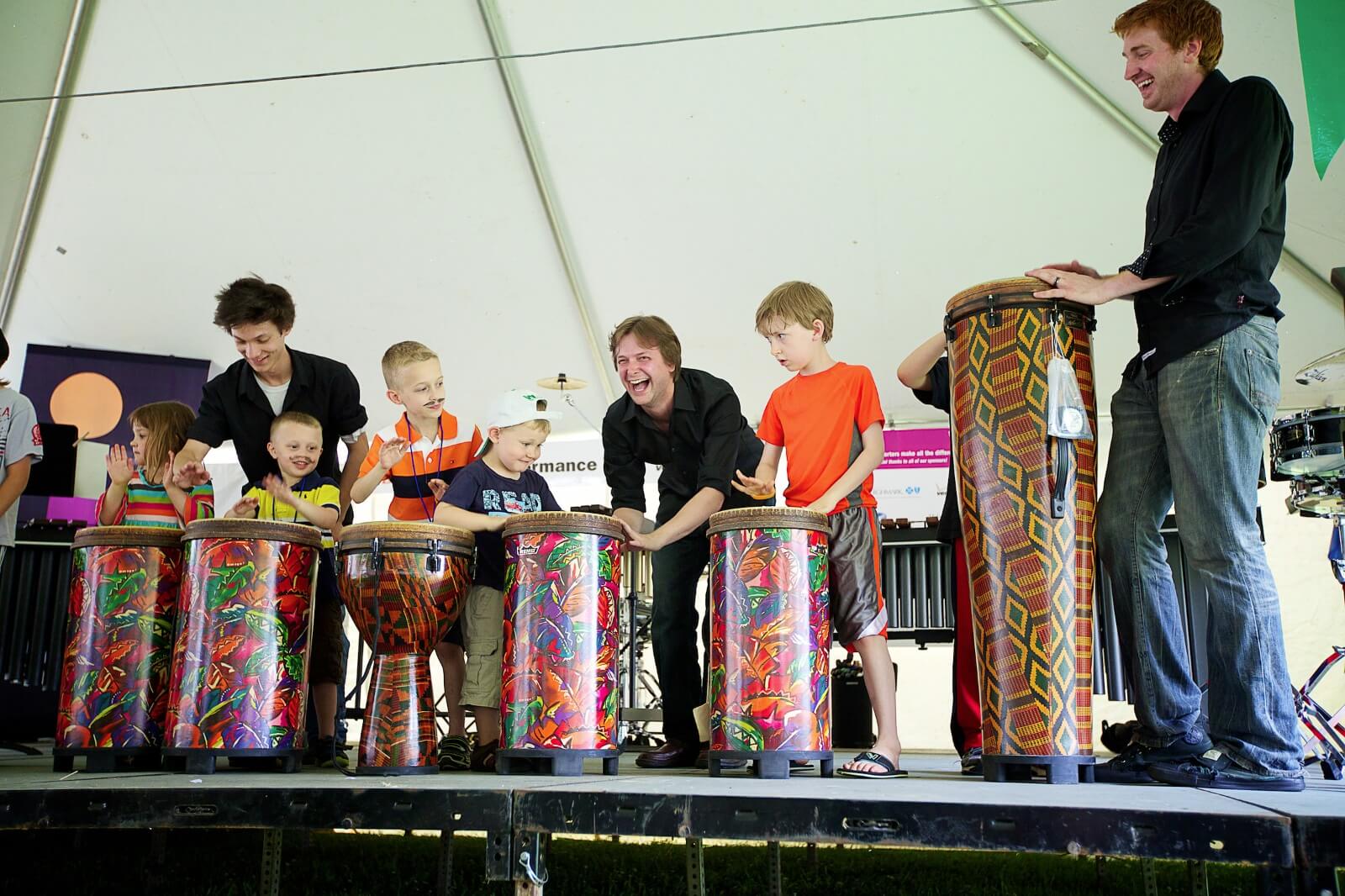 Adults and children learning to play hand drums at the Summer Reading Extravaganza