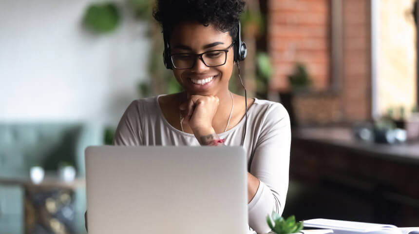 Smiling person wearing headphones while using a laptop.