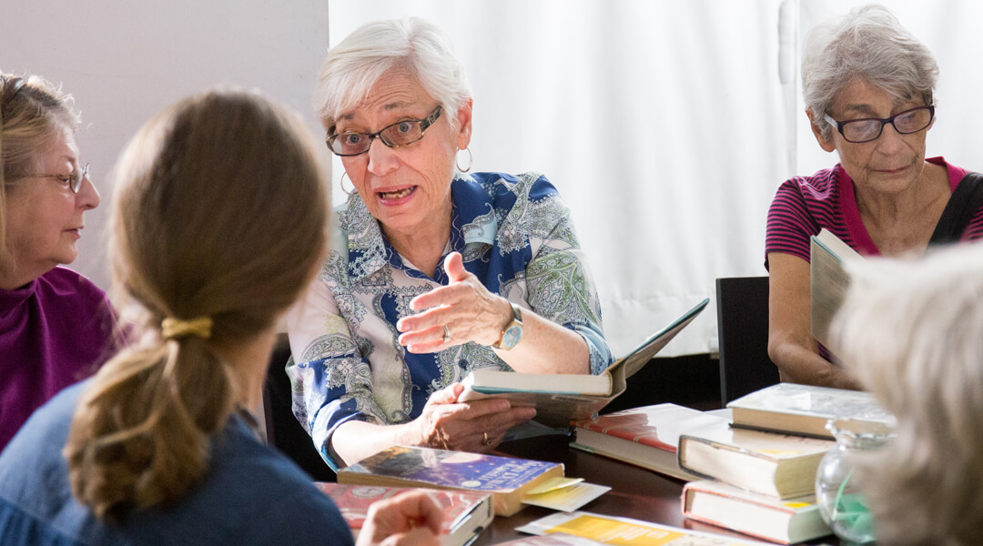 Adults sitting around a table talking with various books.