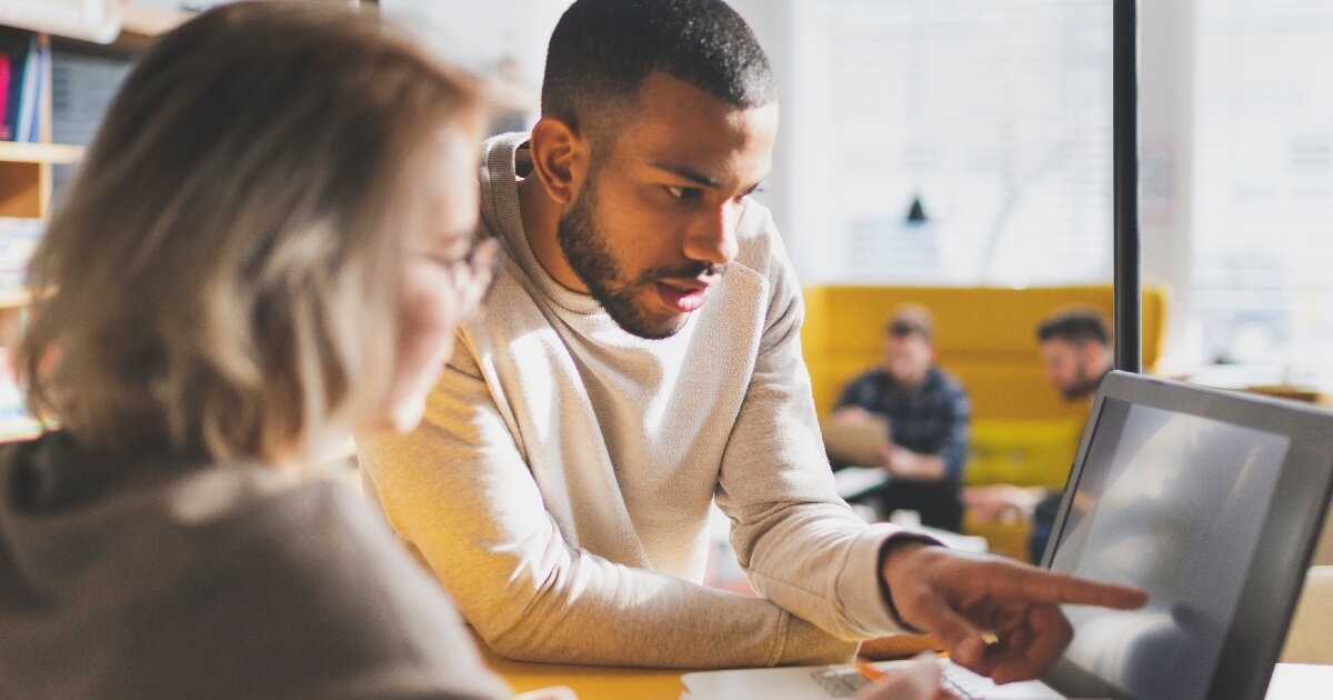 Man with beard showing a woman something on a laptop screen