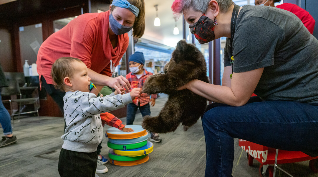 Librarian holding a stuffed animal for a baby to touch.