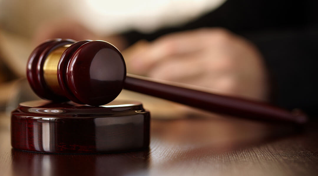 Gavel rests on a judge's desk near their hand.