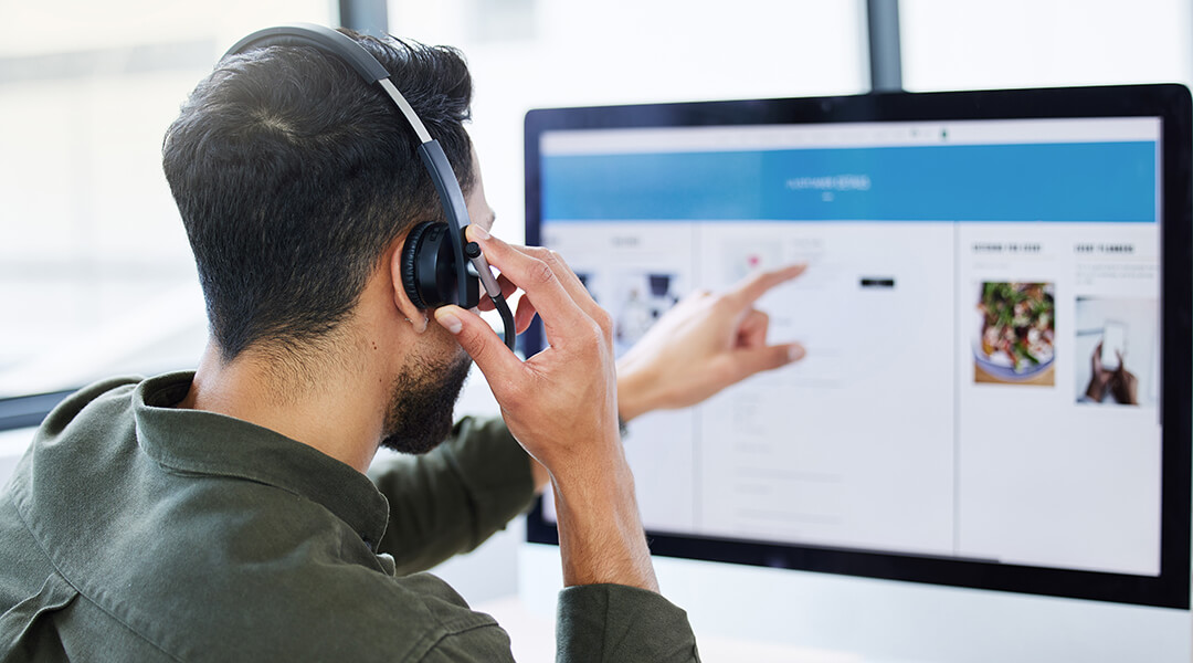 An adult wearing a headset works at a computer.
