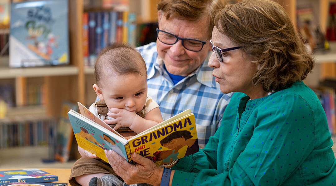 Two grandparents ready a board book to their grandchild
