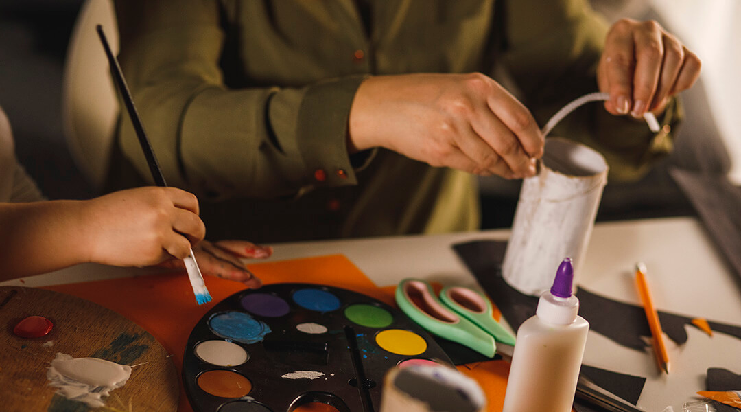High angle view of unrecognizable adult and child sitting at the table together and doing doing arts and crafts.