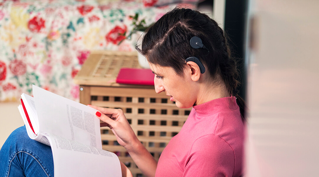 Young adult with cochlear implant reading at home.