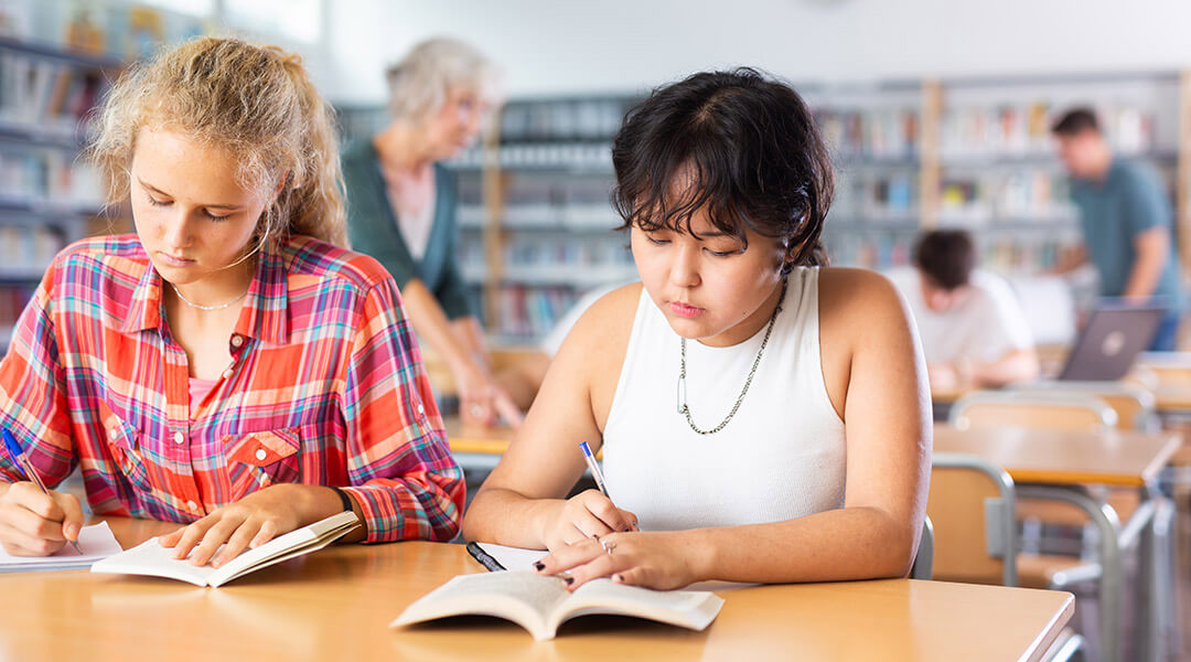 Two high school students study together at the library.