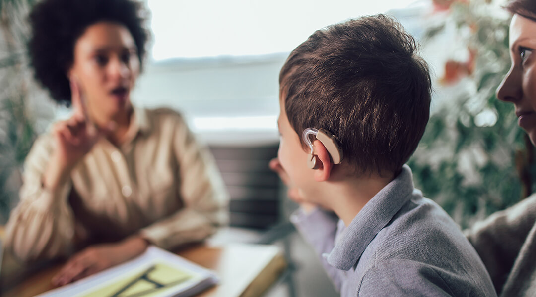 A child wearing a hearing aid learns sign language from an educator.