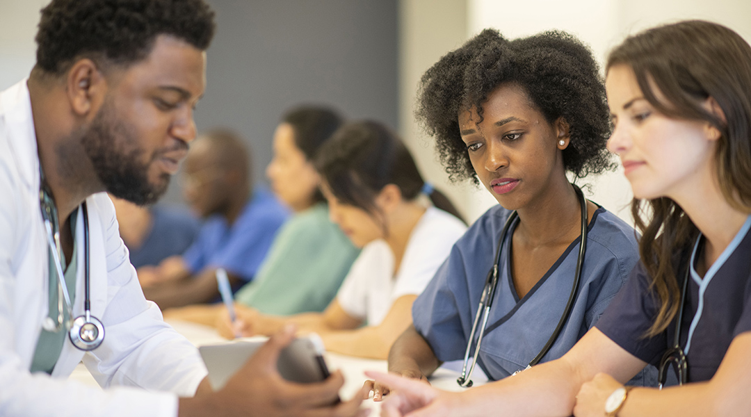 A doctor shares their tablet screen with two of their students.