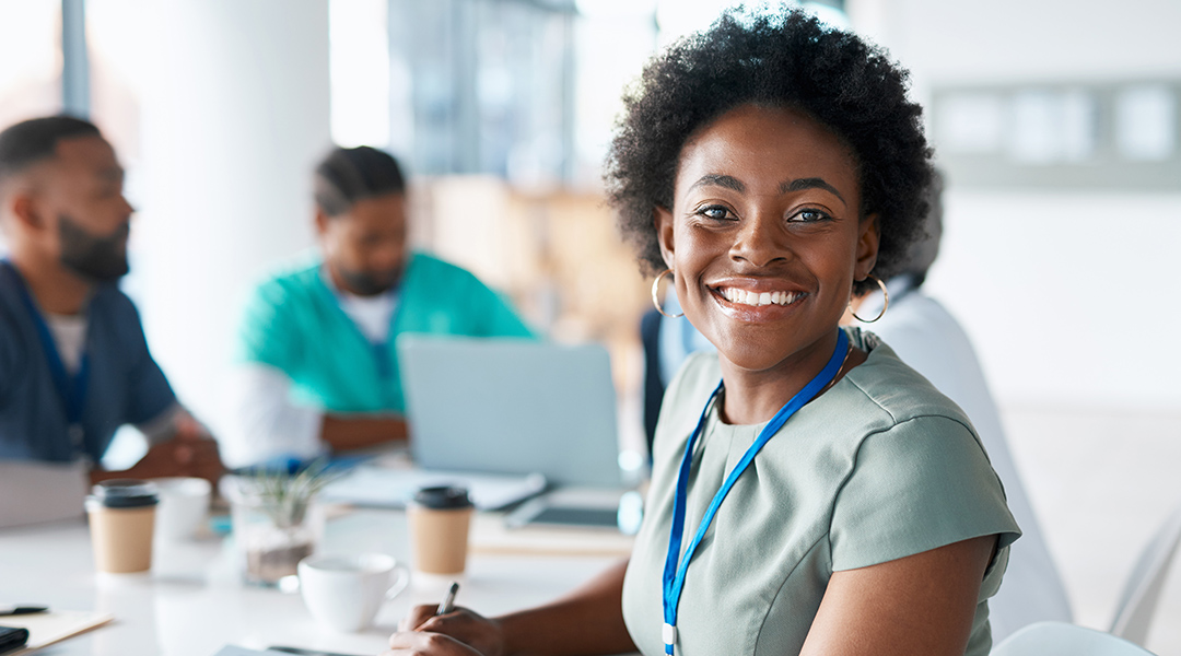 A young professional wearing scrubs smiles during a meeting.