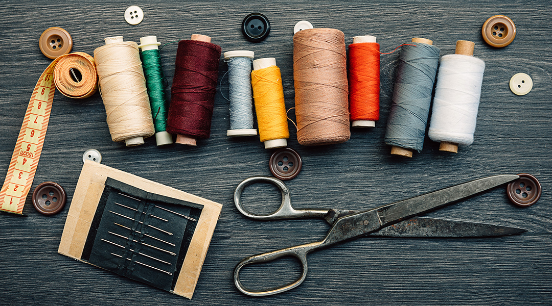 Sewing supplies on a table including thread, buttons, scissors, needles and measuring tape.