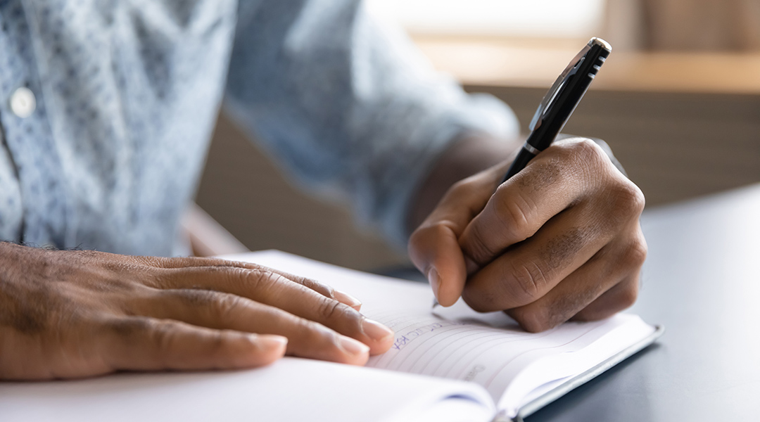 Close up view of left-handed person writing in a notebook.