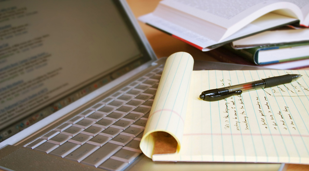A legal pad with hand-written notes resting on top of a laptop keyboard next to open books.