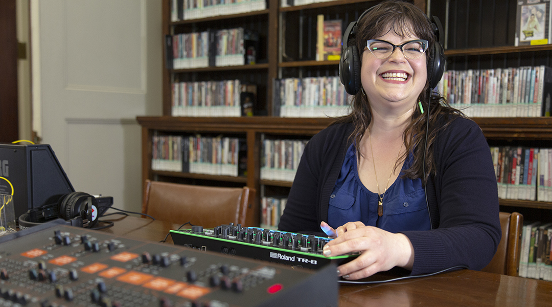A smiling adult wearing headphones uses a piece of musical equipment in MFA.