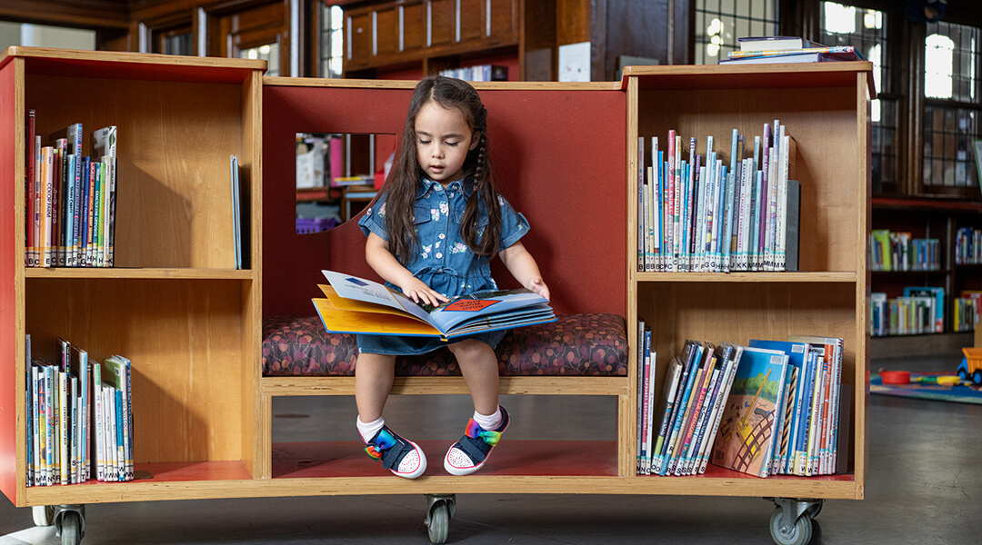 A toddler reads a picture book in the children's space.