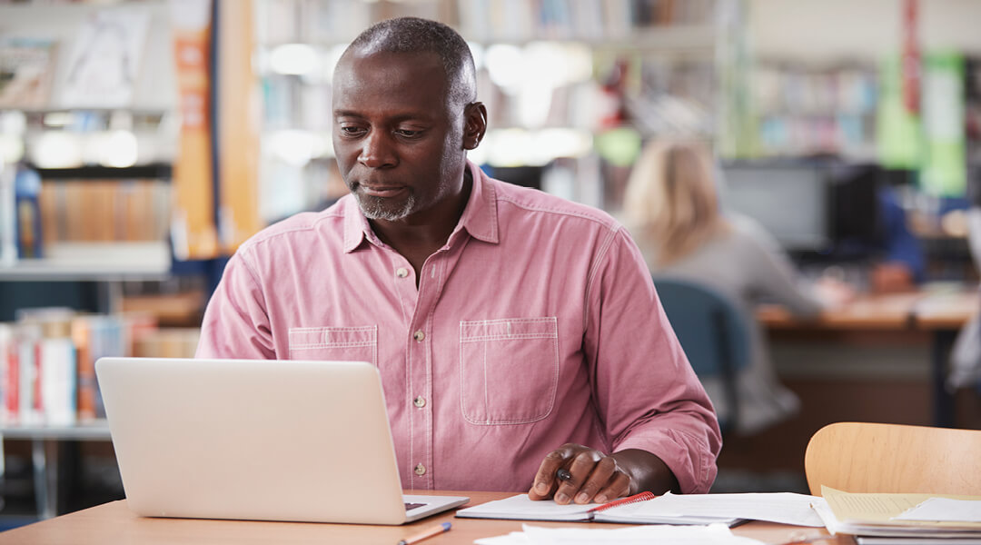 A middle-aged adult uses a laptop in the library.