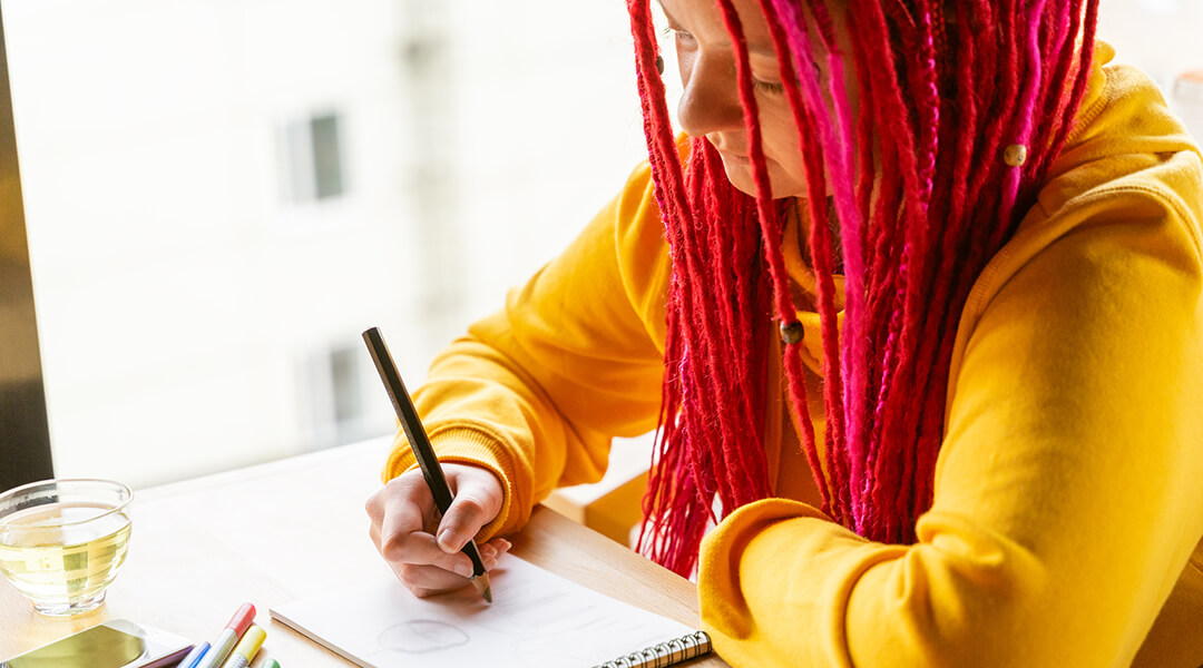 A teenager sits in cafe and draws drawing with colored pencils and markers in notebook.