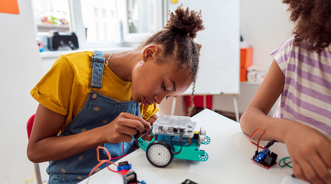 Side view of a child, about ten, programming electric toys and robots at classroom.
