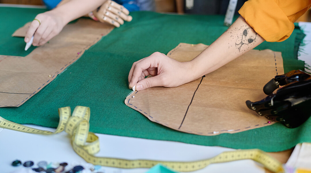 Close up of unrecognizable person with prosthetic hand making clothing and tracing patterns in sewing class.