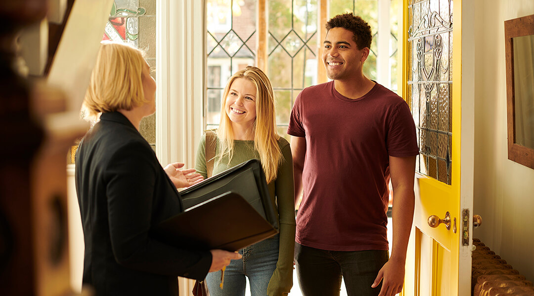 A 20something couple meets with a realtor in the entryway of a house.