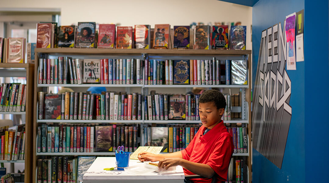 A teenager draws at a desk in the teenspace.