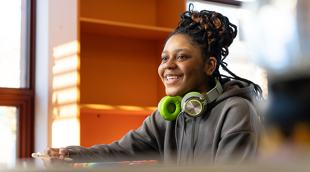 A smiling teenager with headphones around their neck smiles in the teen section.