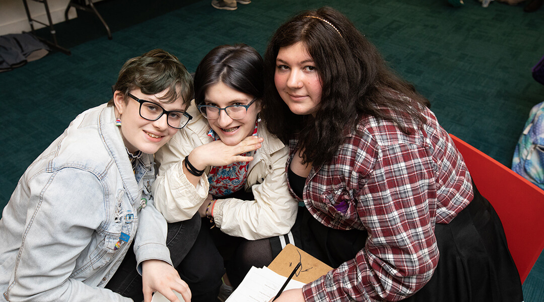 Three young teenagers pose together at a library event.