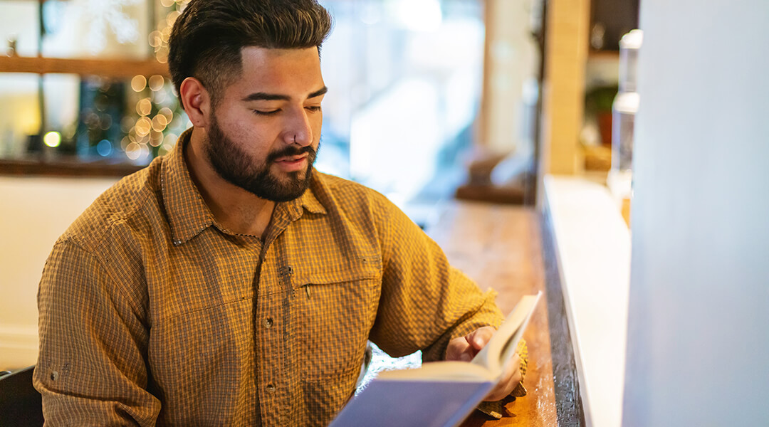 An adult reading a book at a cafe counter.
