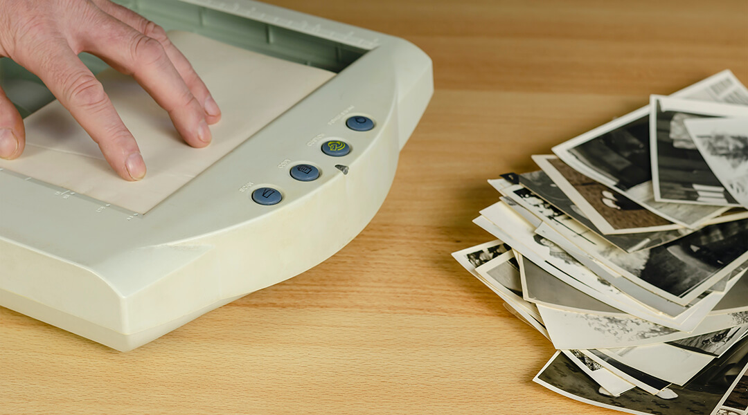 Scanning old photos using a small portable scanner. A hand puts a photo in the scanner. A stack of black and white photos next to each other on the table.