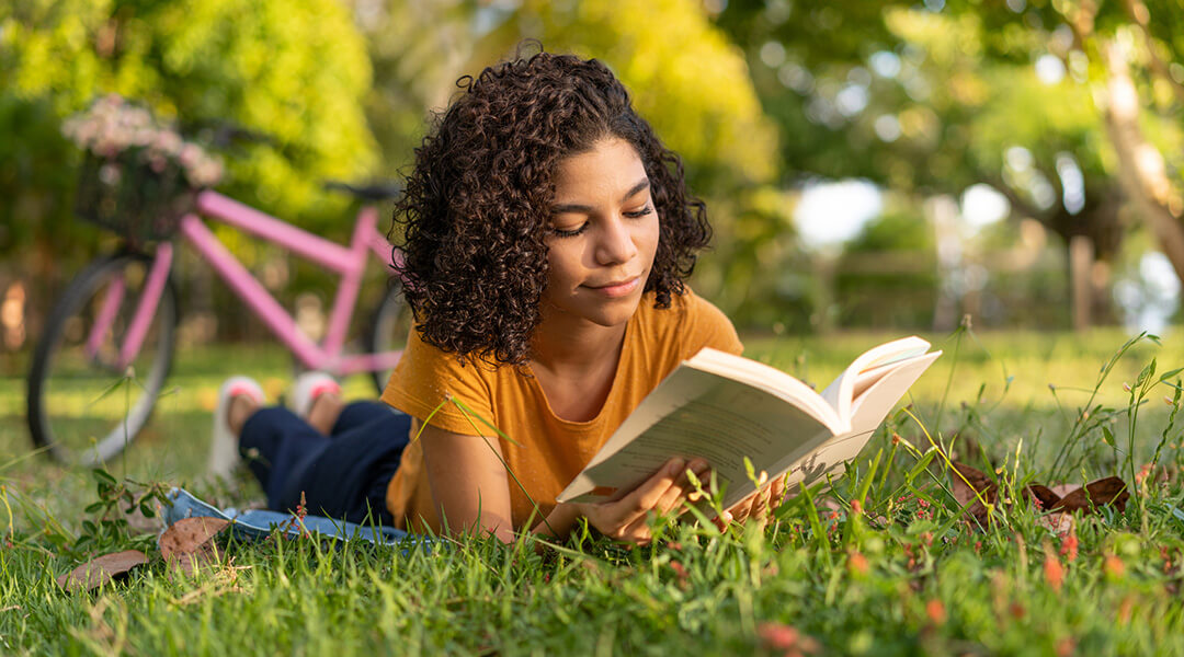 Teen Girl Reading A Book Lying On The Grass