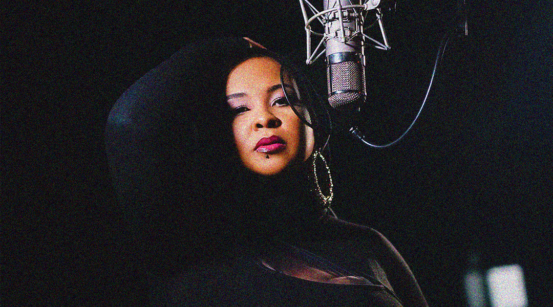Vocalist Kea Michaels posed in a recording studio with a microphone suspended in front of her.