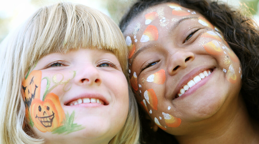 Two young children, about four, smile with Halloween-themed painted faces