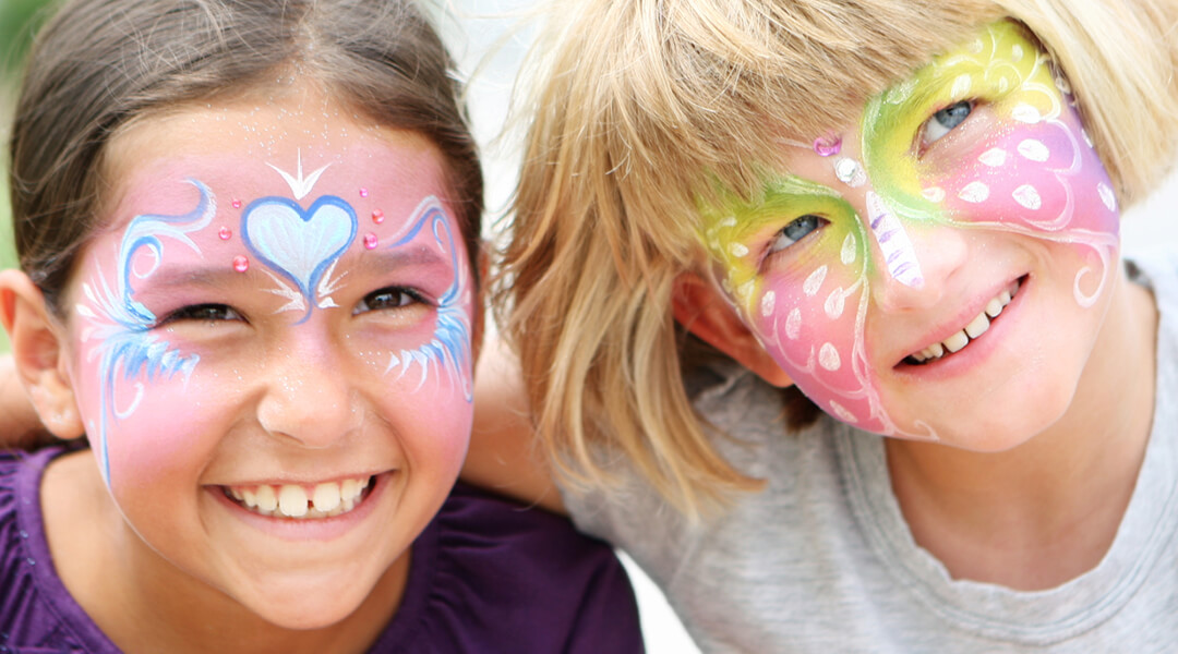 Two children, about six, smile with pastel face paints on their skin.