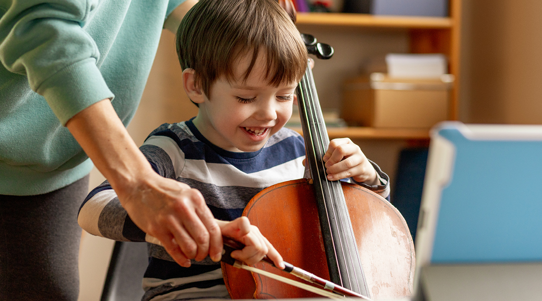 A teacher guides a young child playing the cello.