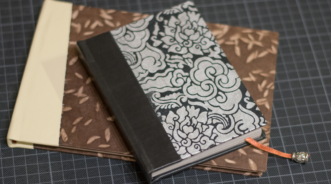 Two hand-bound books with patterned covers and thick binding stacked on a table.
