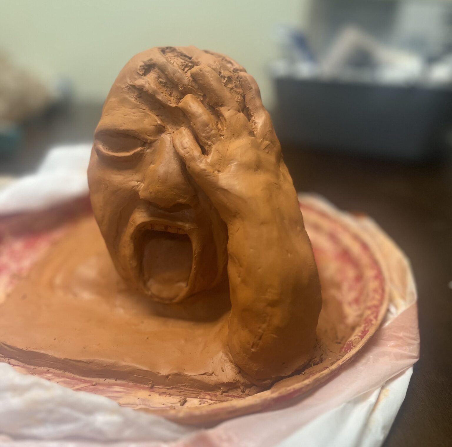 By Jaelyn Gold. A clay bust of a person screaming, hand clutching their head, leaving imprints from where the fingers have dragged across the area.