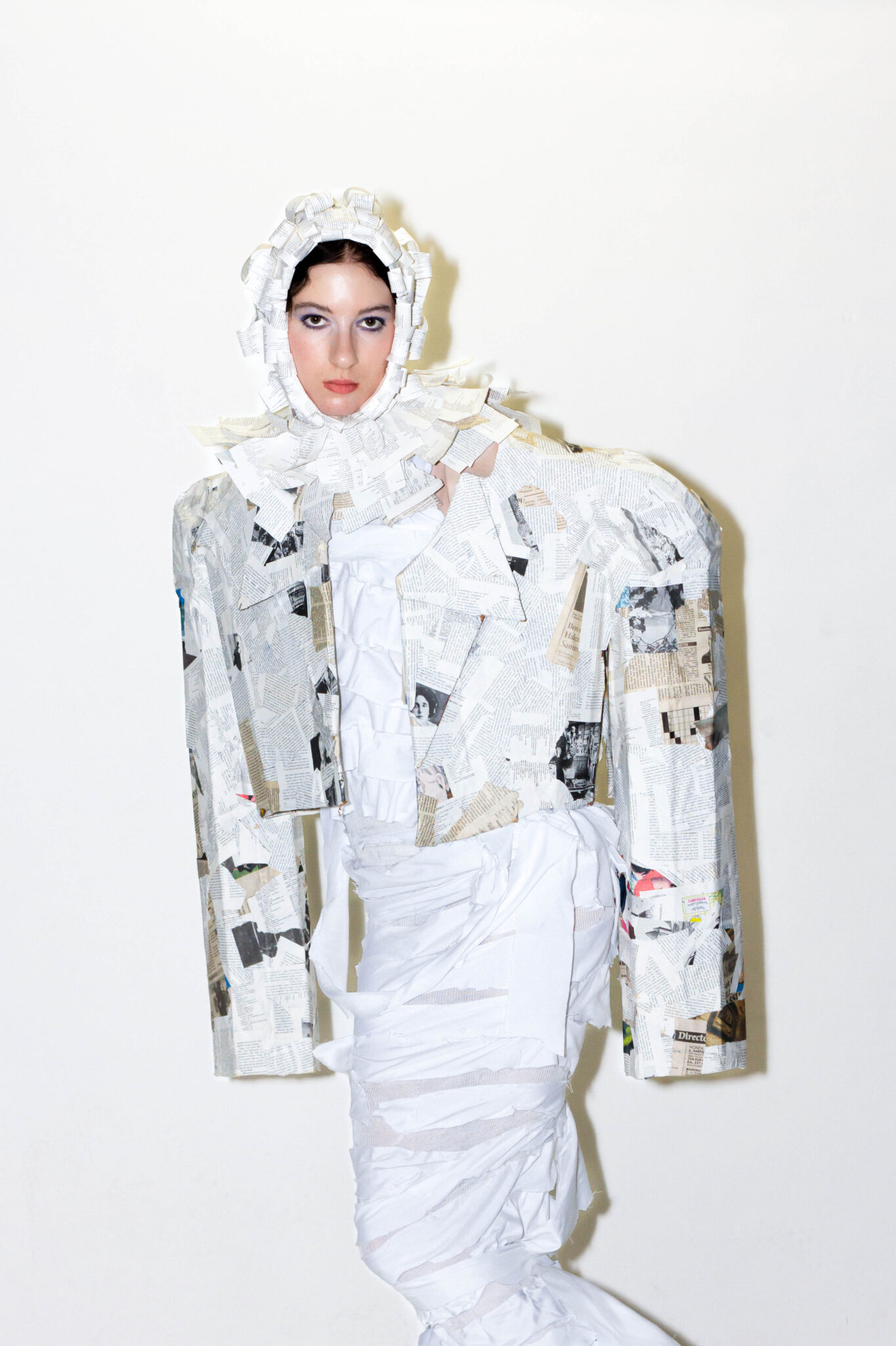 A model poses against a white background wearing a long-sleeved white wrap dress with hood made from recycled materials.