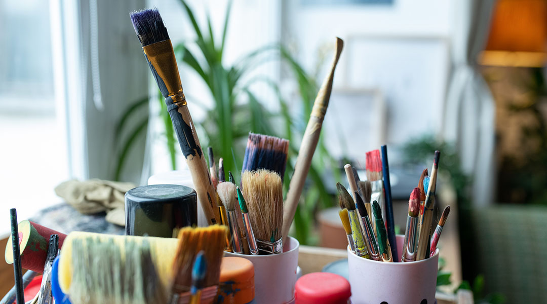 Artists' paintbrushes of various sizes, bristle ends up, in cups.