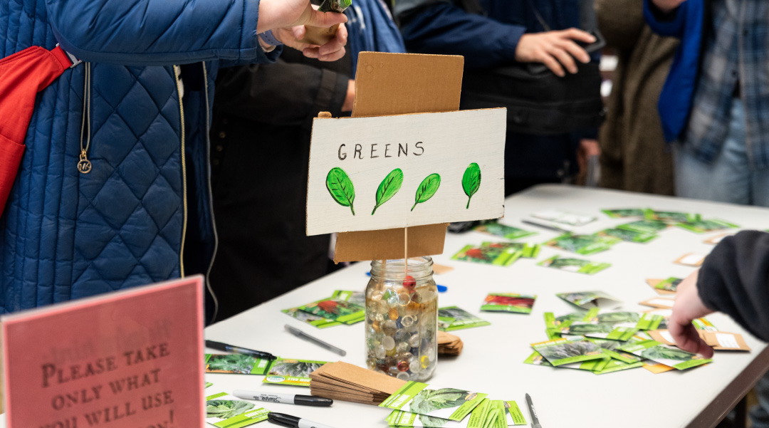 A table with packets of seeds and a hand-made sign reading "greens" with leaf decorations.