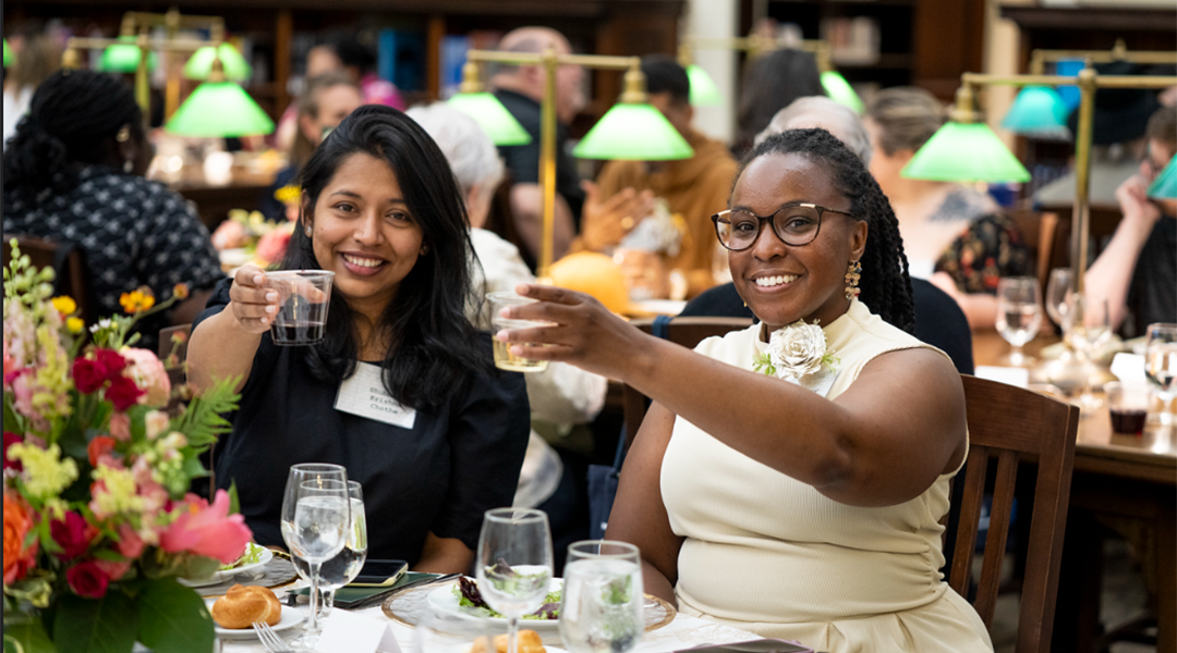 Two people raise their glasses in a toast at a dinner banquet.