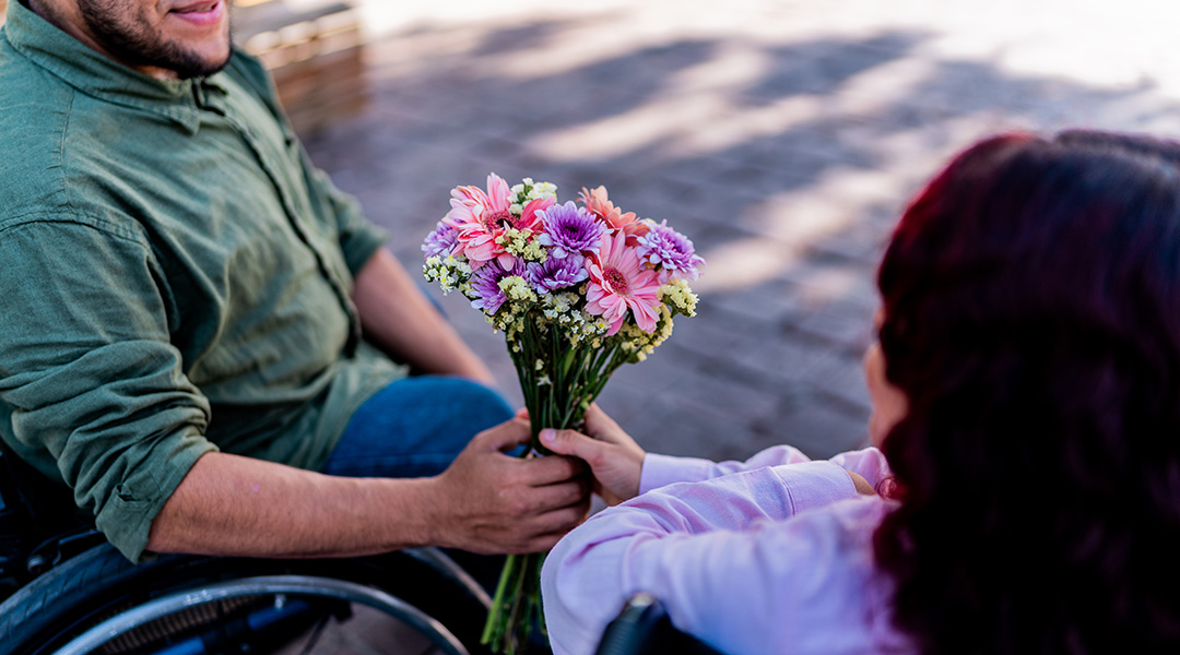 A man gives a woman a bouquet of flowers; both are wheelchair users.