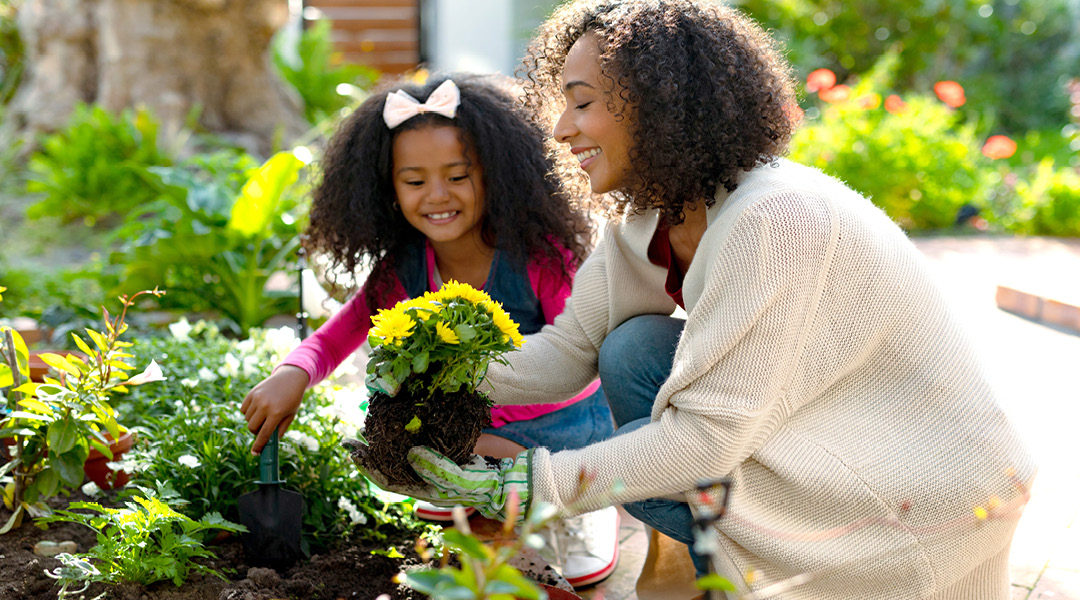 A caregiver and child plant flowers in a garden.