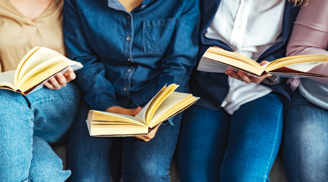 Detail of four adults sitting next to one another, reading books.