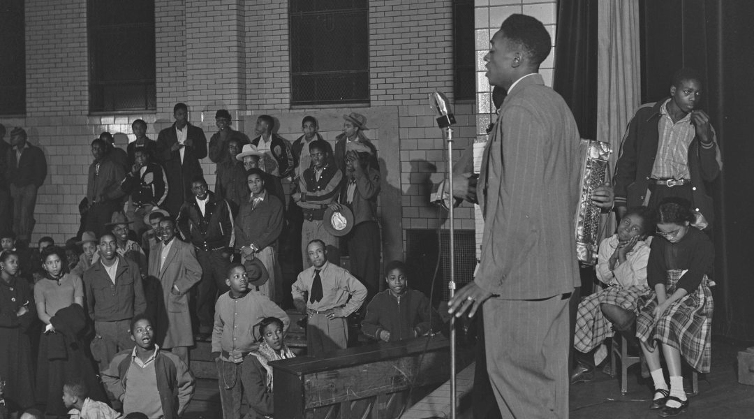 A man sings on stage in front of an audience of adults and children at the Ammon Recreation Center on talent night.