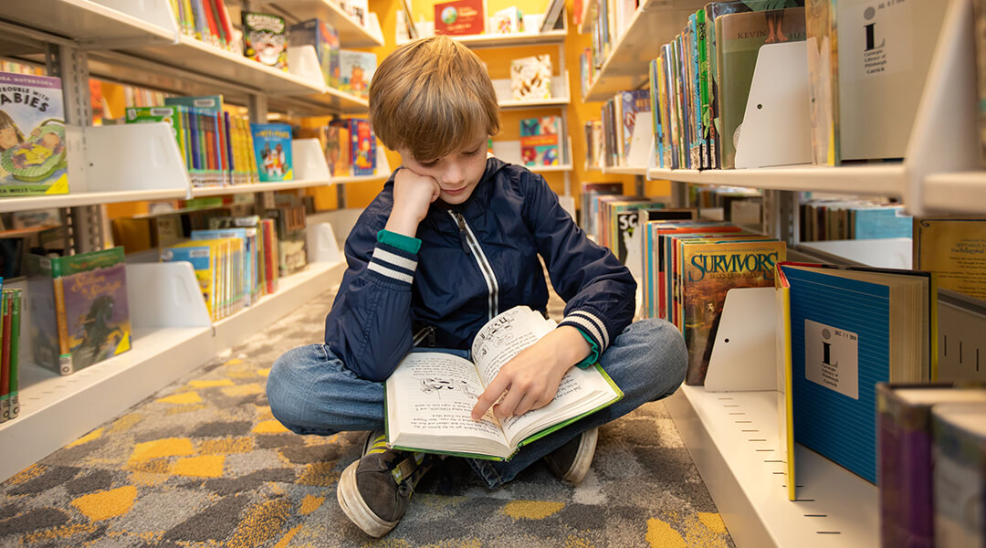 Boy reading a book on the floor of the library