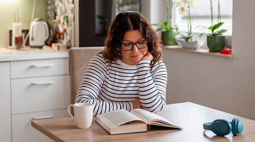 A Woman reading a book in her kitchen.
