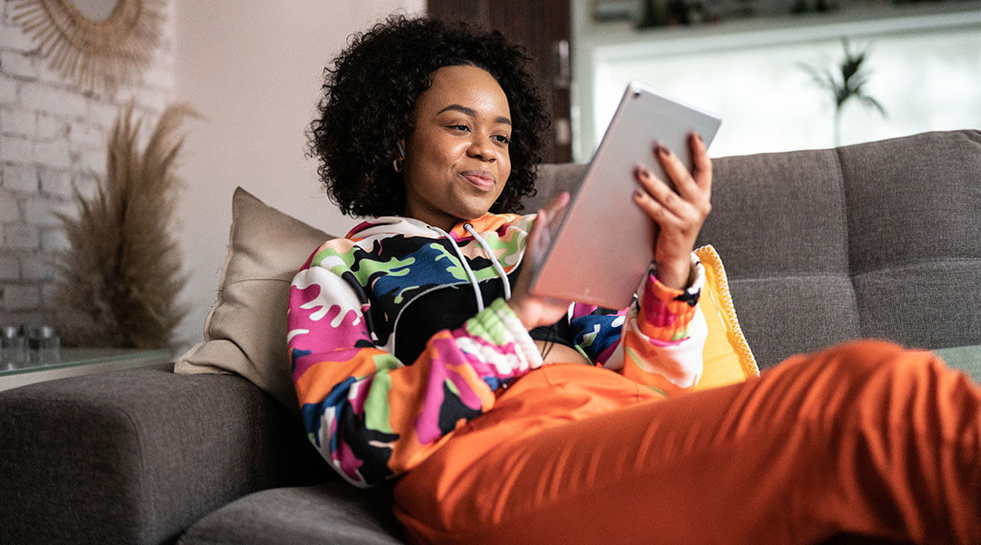 A person sitting on a couch smiles at the tablet in their hands