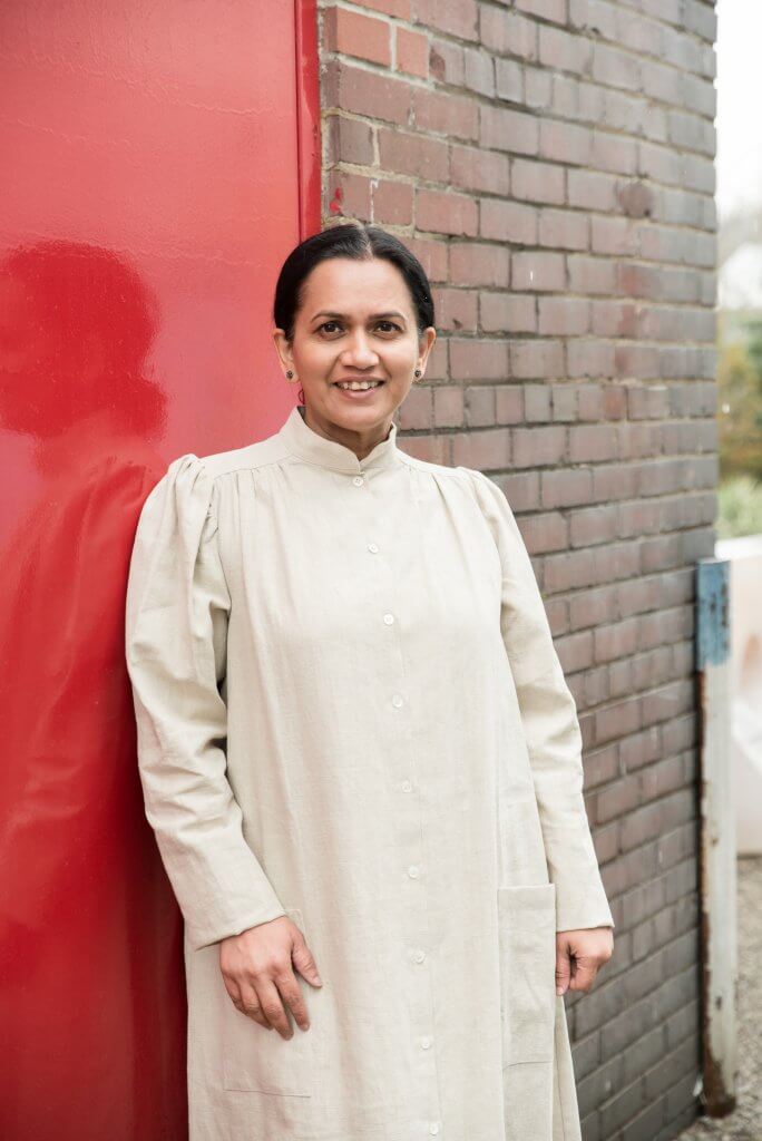 Photo of smiling woman in long off-white dress, standing.