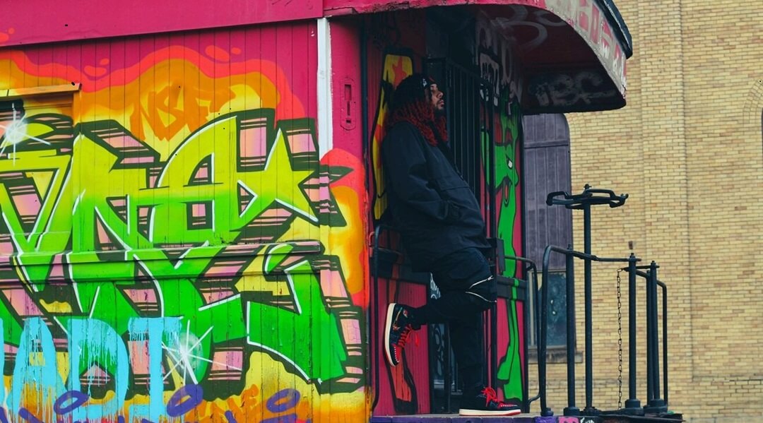 Man standing on the platform of a train marked with colorful graffiti.