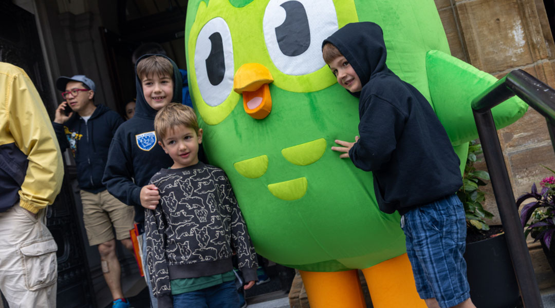 The Duo Lingo mascot taking a picture with several children